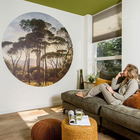Woman sitting on a couch in a living room with a Wallpaper circle of Pine trees in Italy.